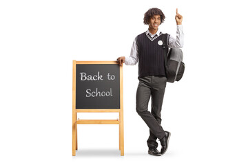 Wall Mural - African american student in a uniform leaning on blackboard with text back to school and pointing up