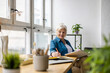 © pikselstock - Smiling mature businesswoman writing in notebook while sitting at table in office