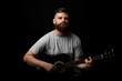 © Volodymyr - Portraite of handsome brunette bearded man musician, guitarist standing and holding a acoustic guitar in a hand and looks in a camera on a black background studio. Ready to play a music.