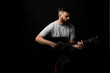 © Volodymyr - Handsome bearded brutal man musician in a grey t-shirt holding a acoustic guitar on a shoulder on black background.