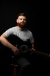 © Volodymyr - Young bearded guitarist in grey t-shirt holds a guitar and playing a song in a dark room.