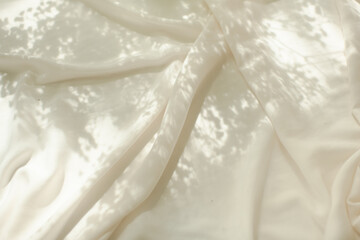 ivory or beige silk or satin fabric with sunlight and shadows of flowers, background photo