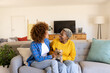© Wavebreak Media - Cheerful diverse lesbian couple with cairn terrier relaxing on sofa in living room, copy space