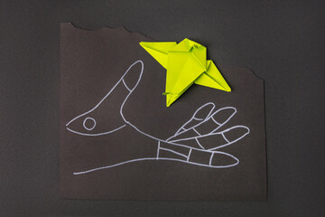 Canvas Print - Drawn hand and green paper bird on black background, top view