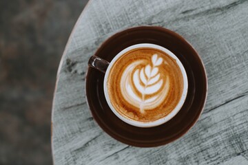 Flat lay or top view shot of a cup of coffee with beautiful Latte Art on wooden table. Blurred background.