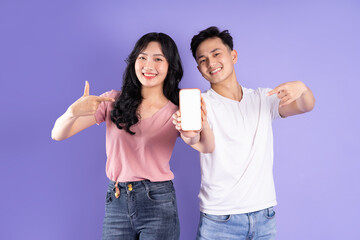 Wall Mural - image of asian couple holding smartphone, isolated on purple background