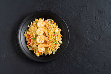 Poster - Fried rice with vegetables and sea prawns, carrots, eggs, and tomatoes. Thai Chinese food is arranged on a black plate on a black background kitchen table, top view.