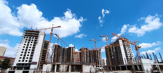 many cranes on building site - construction cranes on blue sky. Residential apartment construction site. Construction site. Big industrial tower cranes with unfinished high raised buildings.