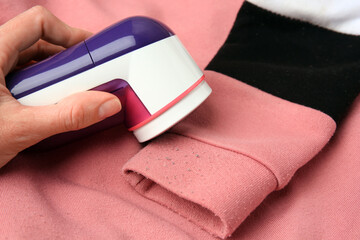 Poster - Woman using modern fabric shaver on sweater with lint, closeup