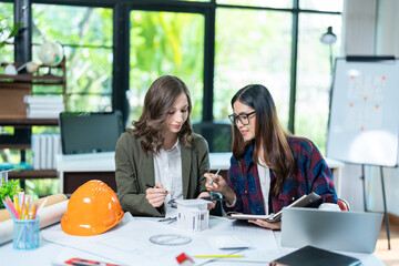 Concept of engineering consulting, Two female engineers discussing about model of building together; Two female architects are studying blueprint of building house.