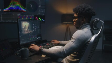 Fototapete - African American film maker or colorist does color grading on computer in studio. Big screen with RGB colour correction graphic bar on the wall. Action film footage displayed on monitor. Dolly shot.