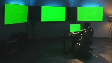 Fototapete - African American colorist works on pc in modern studio with equipment. Multiple chroma key big screens on the wall. Professional software displayed on tablet. Color grading or film montage room.