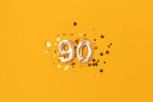 Gold Colored Number 90 And Stars Confetti On A Yellow Background. Festive Glowing Compisition.