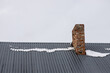 a brick chimney on a metal roof in the winter under the snow. construction concept