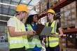 © amorn - Male and female warehouse workers working checks stock and inventory and standing talking together at storage warehouse. Group of warehouse workers discuss and training work in distribution branch