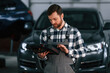 © standret - Holding tablet. Man in uniform is working in the auto salon