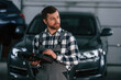 © standret - Holding tablet. Man in uniform is working in the auto salon