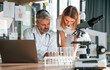© standret - Laptop, test tubes, microscope. Two clinic workers are indoors together. Senior man with young woman