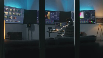 Fototapete - Professional African American video editor makes color grading in program on PC. Process of colour correction for movie post production in modern studio. Multiple monitors with action film footage.