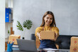 © ArLawKa - Asian businesswoman working with yellow boxes to start online delivery. Freelancer or salesperson checking production orders with laptop. SME entrepreneur making parcel boxes at home.