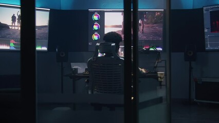 Fototapete - African American colorist does color grading in professional software on computer. Process of colour correction for video post production in modern studio. Multiple monitors with travel movie footage.