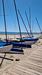 Wall Mural - Yachts and boats on the sand by the sea in spring. A wooden path along the cottages on the shore. Masts of catamarans and yachts against the blue sky. Spain