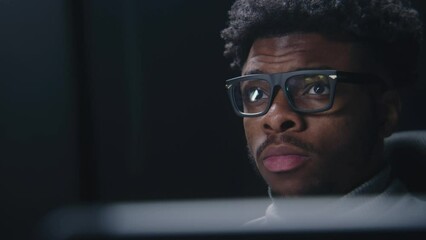 Fototapete - Face close up of African American man working or watching movie in studio with modern design. Film editor looks at monitors. Video footage reflects in the glasses. Freelance and remote work. Zoom in.