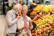 © Dusan Petkovic - An old man is biting fresh apple at the supermarket while his wife is looking at him.