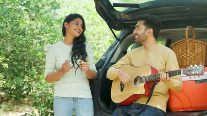 Wall Mural - Girl enjoys boyfriends guitar music while sitting back of car during travel or vacation - concept of dating, holidays and enjoyment.