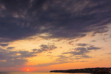 Wall Mural - dramatic dawn at the sea. gray clouds on the sky with red sun above the horizon. summer holidays rai