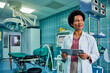 © bnenin - A smiling female African doctor holding a digital tablet and looking outside the window.