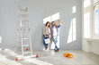 © Studio Romantic - Young family couple doing renovations at home. Happy man and woman painting walls and decorating their house. Husband and wife with bucket and roller standing by wall and discussing interior design