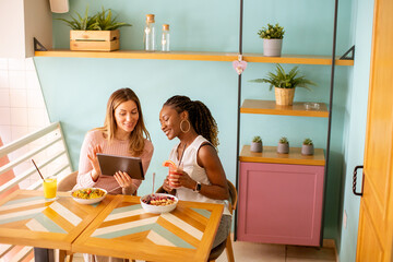 Wall Mural - Young black and caucasian woman having good time, drinking fresh juices and having healthy breakfast in the cafe