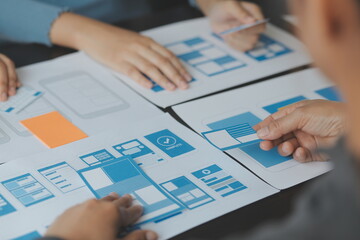 Close up ux developer and ui designer brainstorming about mobile app interface wireframe design on table with customer breif and color code at modern office.Creative digital development agency