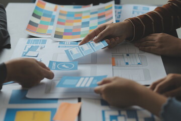 Close up ux developer and ui designer brainstorming about mobile app interface wireframe design on table with customer breif and color code at modern office.Creative digital development agency