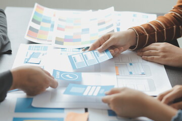 Close up ux developer and ui designer brainstorming about mobile app interface wireframe design on table with customer breif and color code at modern office.Creative digital development agency