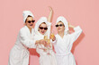 © master1305 - Three beautiful, happy, cheerful girls in bathrobes and towels, drinking champagne, celebrating against pink studio background. Concept of youth, face care, beauty, friendship, hen party, relaxation