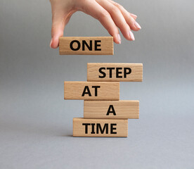 Wall Mural - One step at a time symbol. Concept words One step at a time on wooden blocks. Beautiful grey background. Businessman hand. Business and One step at a time concept. Copy space.