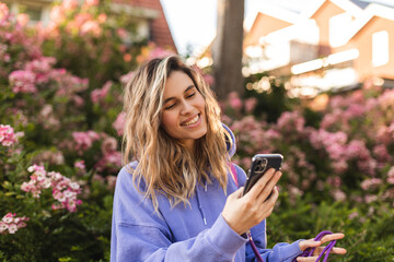 attractive blonde curly woman wear purple hoody hold mobile phone and chatting, messaging, look happ
