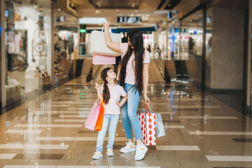 Wall Mural - young mother and daughter holding shopping bags, shopping in the mall. Family shopping.