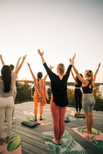 Women With Arms Raised Practicing Yoga On Patio At Sunset