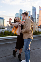 Wall Mural - Happy young beautiful couple on a rooftop just after engagement, marriage proposal showing a ring with a rock on girl hand. Romantic date on Saint Valentine's Day. Urban cityscape on background