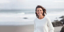 Blissful Beach Portrait Of Smiling 40-year-old Brunette In Light-colored Clothing With Soft-focus Ocean Backdrop. Generative AI