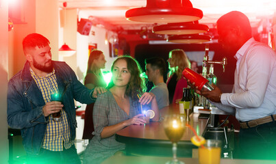 Wall Mural - Portrait of male bartender shaking cocktail mixer for couple in nightclub