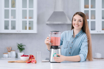 Poster - Beautiful young woman preparing tasty smoothie at white table in kitchen. Space for text