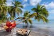 Drink for two on a tropical beach - two glasses of frozen cocktail and a plate of snacks - Caribbean beach with palm trees and white sand
