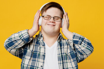 Young smiling satisfied man with down syndrome wears glasses casual clothes headphones listen to music close eyes isolated on pastel plain yellow color background. Genetic disease world day concept.