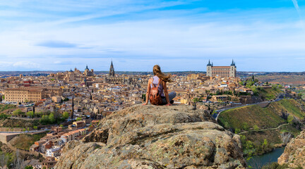 Wall Mural - Woman sitting on rock formation looking at panoramic view of Toledo city landscape in Spain