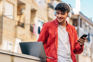 Wall Mural - young man with smartphone or mobile phone, laptop and headphones outdoors in the city