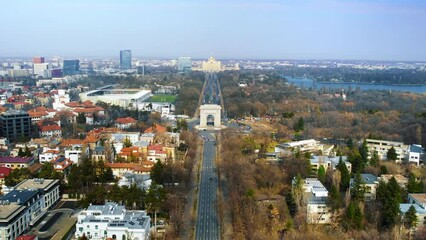 Wall Mural - Aerial drone view of Bucharest, Romania. Triumphal Arch, multiple buildings, moving cars, park with lake and bare trees